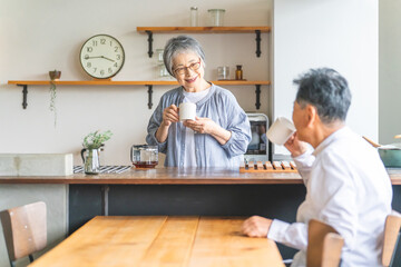 家のダイニング・キッチンでお茶・コーヒーを飲むアジア人高齢者夫婦
