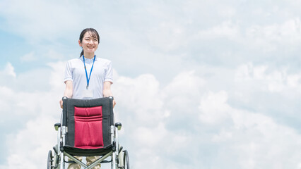 青空の中で車椅子を持つ介護士・作業療法士
