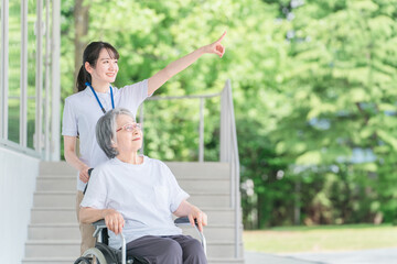 公園を散歩する車椅子に乗った高齢者と介護士（ヘルパー）
