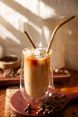 Iced coffee served in a double-walled glass cup and metal straw, a cold summer drink prepared with ice cubes and spices, cinnamon, nutmeg, vanilla, muscovado sugar and cream.