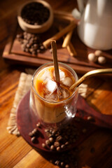 Iced coffee served in a double-walled glass cup and metal straw, a cold summer drink prepared with ice cubes and spices, cinnamon, nutmeg, vanilla, muscovado sugar and cream.