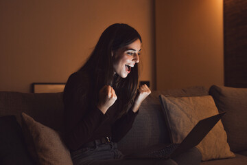 Woman sit at couch read e-mail on laptop makes yes gesture feels happy. Female entrepreneur get...