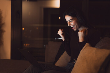 Woman sit at couch read e-mail on laptop makes yes gesture feels happy. Female entrepreneur get...