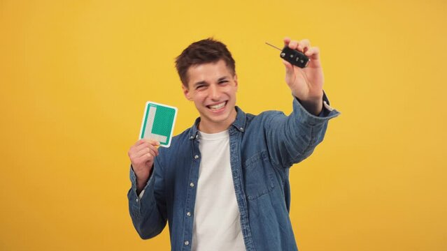 Excited Young Man Holding Car Keys and New Driver L Sign Against a Vibrant Yellow Background. Caucasian guy celebratingt hat he has obtained a driving license at color backdrop. Auto learner man