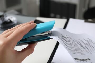 Woman with documents using stapler at white table indoors, closeup