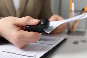 Woman with papers using stapler at white table indoors, closeup