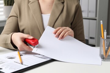 Woman stapling papers at white table indoors, closeup