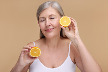 Beautiful woman with halves of orange rich in vitamin C on beige background