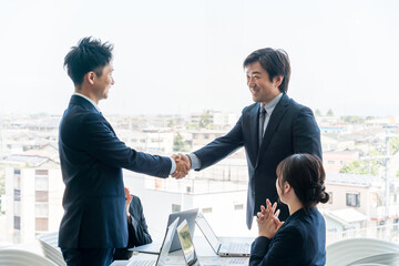 企業のオフィス・会議室で握手をして契約を結ぶビジネスマン
