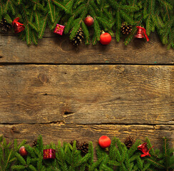 Christmas border with fir tree branches, cones and christmas decorations on rustic wooden boards