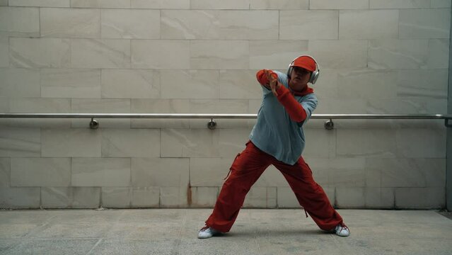 Handsome choreographer practice street dance in gray background. Young attractive b boy dancer perform while wearing stylish cloth. Feeling of lively step. Copy space. Outdoor sport 2024. Sprightly.