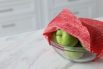 Apples in bowl covered with beeswax food wrap on white table, closeup. Space for text