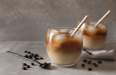 Refreshing iced coffee with milk in glasses, beans and spoon on gray table, closeup. Space for text