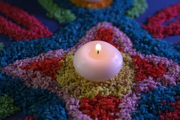 Diwali celebration. Burning candle and colorful rangoli on table, closeup