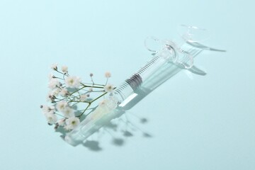 Cosmetology. Medical syringe and gypsophila on light blue background
