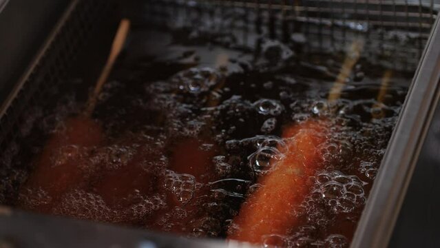 Cooking corn dogs in boiling oil close-up. Traditional asian corndog snacks street food. Fried sausage in breadcrumbs on a stick. Korean Chinese street local market with traditional food. American