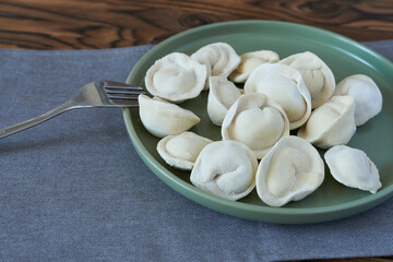 Fototapeta na wymiar Dumplings in a plate. Frozen dumplings in green plate on wooden table with fork. The concept of making lunch.