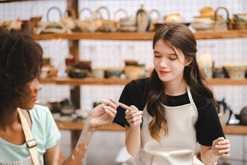 Two multi-ethnic friend is enjoy a having fun while learning a pottery or sculpture workshop,...