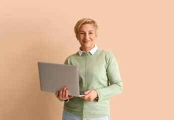 Mature female programmer with laptop on beige background