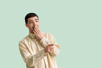 Surprised young man pointing at something on green background