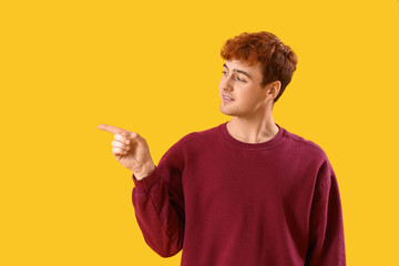Young redhead man pointing at something on yellow background