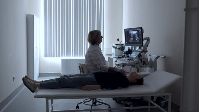 Ultrasound diagnosis of the thyroid gland of a young woman in the clinic. Clip. A female doctor holds an ultrasound probe.