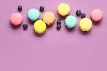 Different sweet macaroons and blueberries on purple background