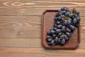 Tray with sweet black grapes on wooden background