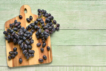 Board with sweet black grapes on green wooden background