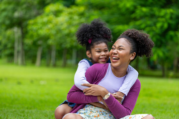 African American mother is playing piggyback riding and hugging with her young daughter while...