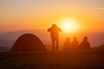 Group of friends sitting by the tent during overnight camping while looking at the beautiful view point sunset over the mountain for outdoor adventure vacation travel concept