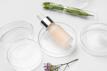 Petri dishes with herbs and bottle of cosmetic product on white background