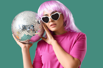 Stylish young woman in wig with disco ball on green background