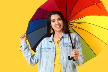 Beautiful happy young woman with umbrella on yellow background