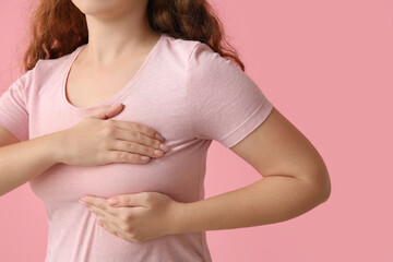 Young woman checking her breast on pink background, closeup. Cancer awareness concept