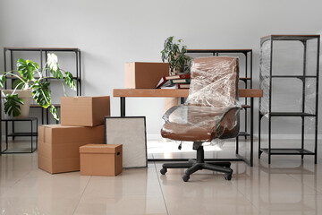 Interior of office with chair wrapped in stretch film and cardboard boxes on moving day - obrazy, fototapety, plakaty