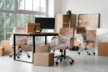 Interior of modern office with chairs wrapped in stretch film and cardboard boxes on moving day