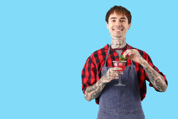 Young male bartender with glass of cocktail on blue background