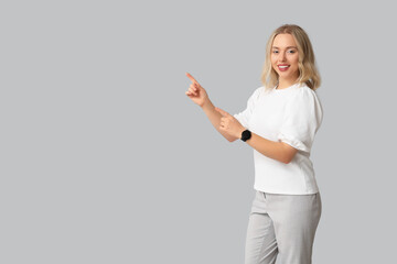 Pretty young woman with modern smartwatch pointing at something on grey background