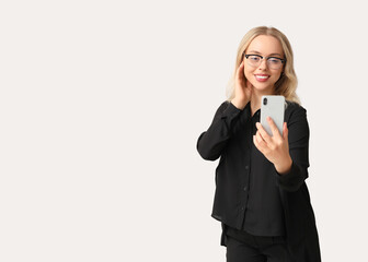 Obraz premium Smiling young business woman in eyeglasses using smartphone for video call or selfie isolated on light background with copy space