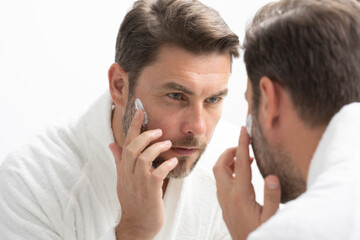 A man observes his face in the mirror, examining his jaw, ear, and eyelashes. His happy expression reflects contentment, sharing the art of self-reflection.