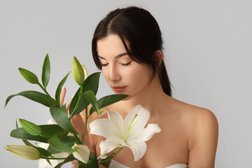 Beautiful young woman with white lily flowers on grey background, closeup