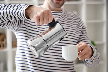 Man pouring espresso from geyser coffee maker into cup in living room, closeup