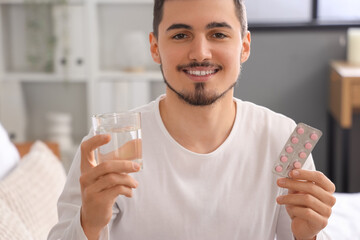 Young man with pills and glass of water in bedroom