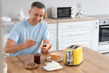 Middle-aged man having sweet jam toasts for breakfast in kitchen - obrazy, fototapety, plakaty