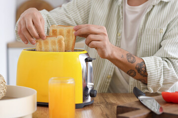 Young man making crispy toasts in kitchen, closeup