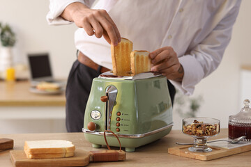 Young man taking crispy toasts from toaster in kitchen, closeup - obrazy, fototapety, plakaty