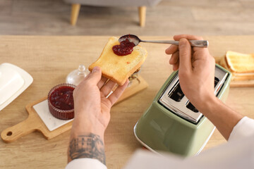 Young man making sweet jam toast for breakfast in kitchen, closeup