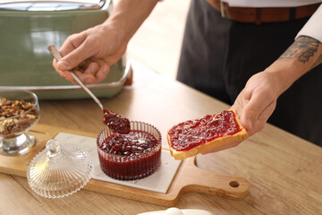 Young man making sweet jam toast for breakfast in kitchen, closeup
