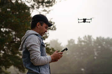 Professional photographer taking photos from drone. Young man taking aerial photos in forest. Man controlling his drone on background of mountain forest.